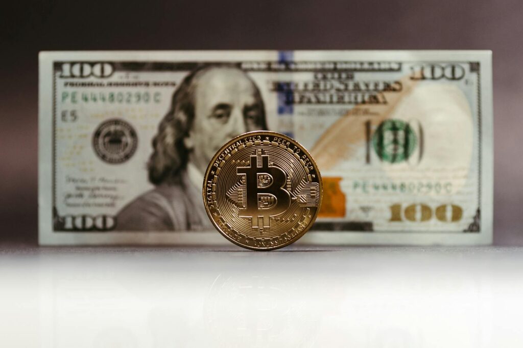 Close-up of a Bitcoin coin placed in front of a US hundred-dollar bill, highlighting cryptocurrency versus traditional money.