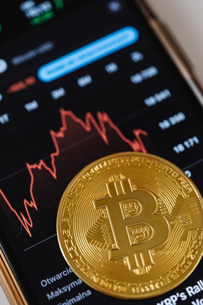 Gold Bitcoin coin on a smartphone showing financial graph, symbolizing digital currency and blockchain trends.