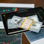 Stack of $100 bills placed on a tablet with financial graphs, symbolizing digital finance.