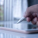 a person holding a pen and writing on a tablet