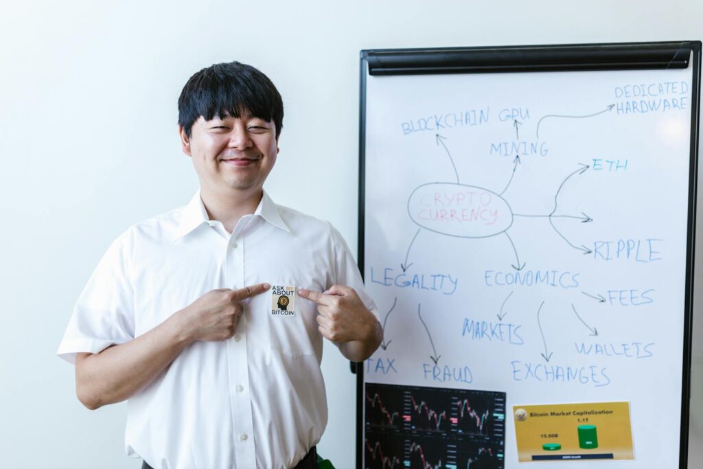 Smiling businessman pointing at Bitcoin badge in front of whiteboard with cryptocurrency concepts.