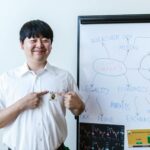 Smiling businessman pointing at Bitcoin badge in front of whiteboard with cryptocurrency concepts.