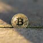 A golden bitcoin coin rests on a textured surface.